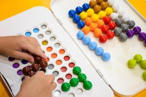 Top view of a child hand playing Jumbo beads puzzle on yellow background, kids playing 3D logic IQ beads puzzle, Children playing with colorful puzzle beads in the classroom for learning and skills. photo