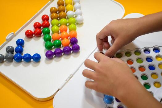 Close up of a child hand playing Jumbo beads puzzle on yellow background, kids playing 3D logic IQ beads puzzle, Children playing with colorful puzzle beads in the classroom for learning and skills. photo