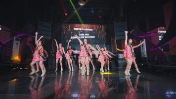 Group of dancers performing on stage with colorful lighting and a digital screen in the background. video