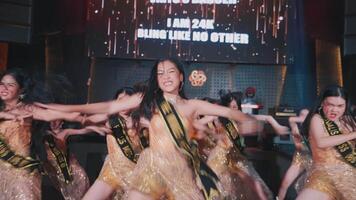 Group of dancers performing energetically on stage with dynamic lighting and a vibrant backdrop, showcasing synchronized dance video
