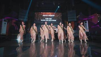 Group of energetic dancers performing on stage with dynamic lighting and a vibrant backdrop, showcasing modern dance video