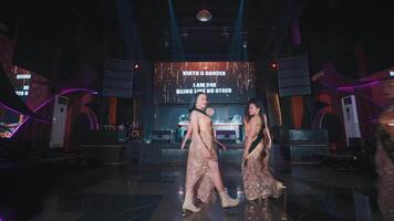 Group of dancers performing on a club stage with vibrant lighting and a digital screen displaying text in the background video