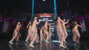 Group of dancers performing on stage with dynamic lighting and a digital screen displaying text in the background video