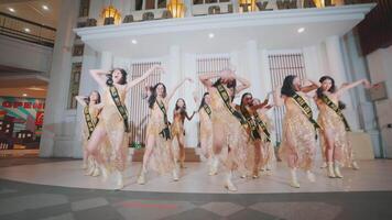 A dynamic group of female dancers performing in golden costumes with a modern indoor setting as a backdrop video