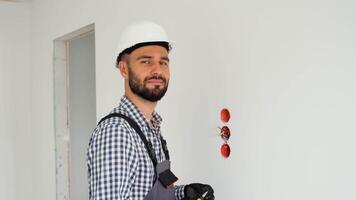 Portrait of electrician in uniform while replacing a socket in apartment after renovation work video