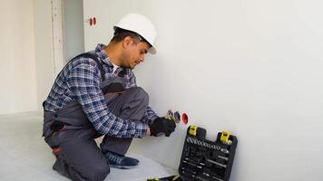Indian electrician in uniform using pliers while replacing a socket in apartment after renovation work video