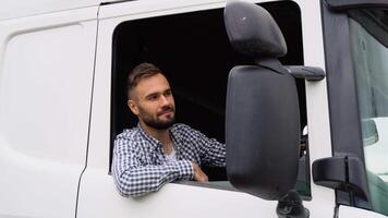 A driver sitting inside the semi-truck while looking at camera through the open window. Right hand drive car video