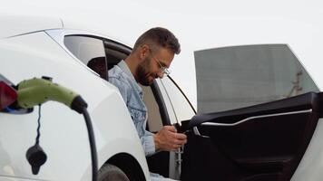 Bearded man with smartphone waiting for the finish of the battery charging process of electric car video