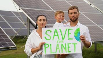 Save the planet with solar energy. Three people holding a sign SAVE THE PLANET in front of a solar panel farm video