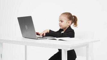 A cute little girl in front of a laptop experiences emotions from an idea or solution to a problem, the girl uses a computer for distance learning on a light background. video