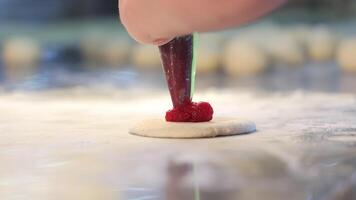 A chef uses a pastry bag to squeeze raspberry filling onto a piece of dough, close-up. Cookie baking concept video