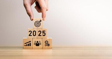 Hand Stacking Wooden Blocks with 2025 Year, Target, Growth, Teamwork, and Innovation Icons, Representing Strategic Business Goals, Future Planning, Organizational Development, and Corporate Success photo