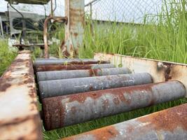 A close-up view of an aged, rusted roller conveyor, partially obscured by lush green grass, evokes a sense of industrial history and the passage of time. photo