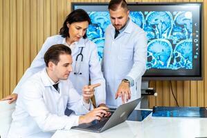 Team of three doctors discusses the results of an MRI scan of the patient's head in the consulting room of modern hospital, physician discussing about treatment for patient looking in laptop photo