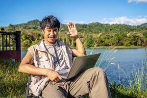 Young travel man relax and enjoy talking calling on on laptop, using laptop computer work remotely anywhere using internet connected to portable solar panel charging photo