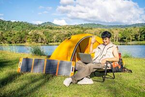 Young travel man relax and enjoy talking calling on on laptop, using laptop computer work remotely anywhere using internet connected to portable solar panel charging photo