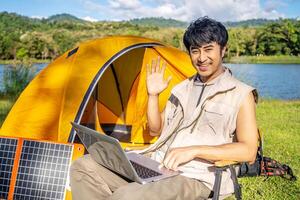Young travel man relax and enjoy talking calling on on laptop, using laptop computer work remotely anywhere using internet connected to portable solar panel charging photo