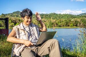 Young travel man relax and enjoy talking calling on on laptop, using laptop computer work remotely anywhere using internet connected to portable solar panel charging photo