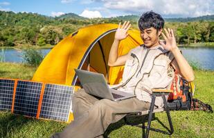 Young travel man relax and enjoy talking calling on on laptop, using laptop computer work remotely anywhere using internet connected to portable solar panel charging photo