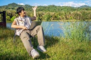 Young travel man relax and enjoy talking calling on on laptop, using laptop computer work remotely anywhere using internet connected to portable solar panel charging photo