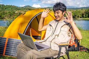 Young travel man relax and enjoy talking calling on on laptop, using laptop computer work remotely anywhere using internet connected to portable solar panel charging photo
