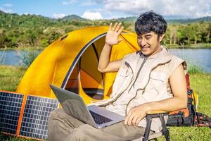Young travel man relax and enjoy talking calling on on laptop, using laptop computer work remotely anywhere using internet connected to portable solar panel charging photo