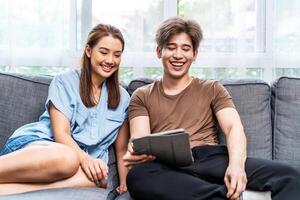 Portrait of an happy couple in love using a tablet, looking at digital computer tablet screen, relaxing on comfortable couch. Loving couple shopping online in internet store. photo