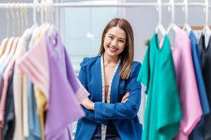 Beautiful woman business owner choose clothes in the clothes rail, Fashion designer standing and smile in cross arm gestures during working at fashion studio, Concept Professional Dressmaker designer photo