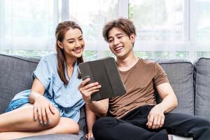 Portrait of an happy couple in love using a tablet, looking at digital computer tablet screen, relaxing on comfortable couch. Loving couple shopping online in internet store. photo