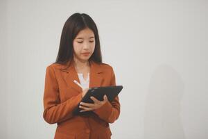 Young beautiful Asian woman in business office standing use tablet in hand, Thai girl enjoy browsing for online shopping store with copy space for advertisement, on isolated white background photo