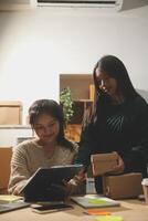 Startup small business SME, Entrepreneur owner African woman using smartphone or tablet taking receive and checking online purchase shopping order to preparing pack product box. photo
