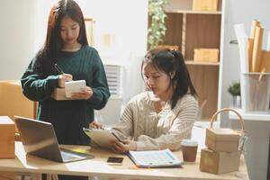 Startup small business SME, Entrepreneur owner African woman using smartphone or tablet taking receive and checking online purchase shopping order to preparing pack product box. photo