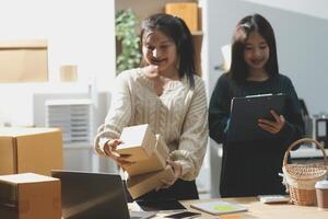 Startup small business SME, Entrepreneur owner African woman using smartphone or tablet taking receive and checking online purchase shopping order to preparing pack product box. photo