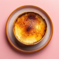 Closeup of a delicious creme brulee dessert with a crispy caramelized sugar topping served on a plate, isolated on a pink background. photo
