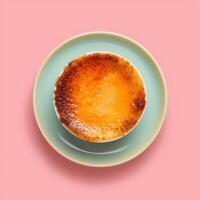 Overhead view of a delicious creme brulee dessert with a crispy caramelized sugar crust, served in a white ramekin on a blue saucer on a pink background photo