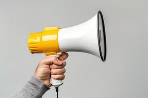 Hand holding a yellow and white megaphone on a gray background photo