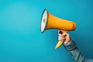 Hand holding a bright yellow megaphone against a blue background photo