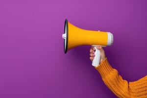 Hand holding a yellow megaphone against a purple background photo