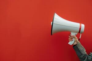 Hand holding a megaphone against a red background photo