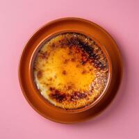 Close up of a creamy Creme Brulee with a perfectly caramelized sugar crust, served on a pink saucer with a pink background. photo