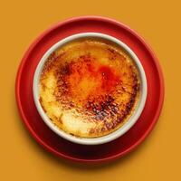 Close up of creme brulee dessert with crispy caramelized sugar topping on a white ramekin with red plate. Delicious homemade dessert with golden brown crust. photo