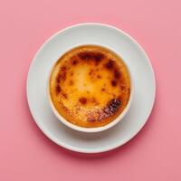 Close up of a creamy Creme Brulee with a perfectly caramelized sugar crust, served on a pink saucer with a pink background. photo