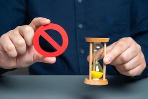 A man holds a red NO sign and an hourglass. Time is running out. Deadline approaches. Important prohibition must be adhered to without delay. Temporary restriction for a limited time. photo