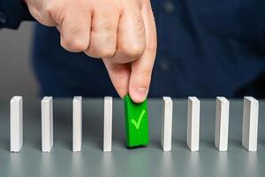A man holds a green domino with a check mark. Checkpoint reached, milestone. Successfully completed. Ready for launch. Checking and verification. Start a business. A life stage that has been passed. photo