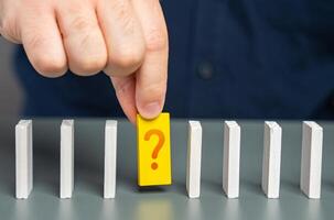 A man studies an unknown element of a chain of processes in the form of dominoes. Finding an answer to a question. Mistake correction. The fact remains in question. An unknown issue photo