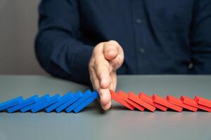 A man stops two domino chains from colliding. The concept of stopping a conflict and preventing further escalation. Elections and confrontation of the parties. Mentoring. Find points of compromise. photo