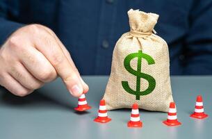 A man surrounds a dollar money bag with cones. Financial restrictions and sanctions. Freezing of capital, seizure of funds. Limitation on use of dollar transactions. Regulatory budget spending policy photo