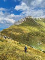 Solo traveling backpacker hiking on trail against backdrop of summer mountain landscape with Prutas summit in Durmitor National Park, Montenegro. Man walking on a trail in mountainous green valley. photo