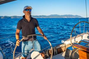 Young man captain stands at the helm and controls a sailboat during a journey by sea. High quality photo