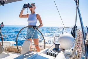 Young female captain on the yacht looking through binoculars during sailing boat control. Travel and active life. Yachting. High quality photo